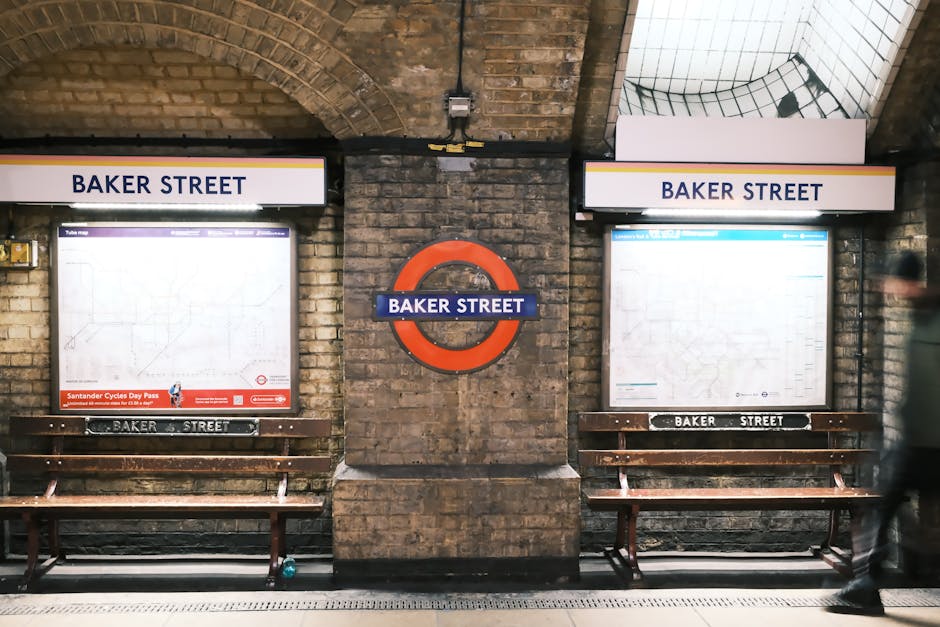 The open doors of a London Underground train at Bounds Green station reveal the interior with two blue upholstered seats, grab handles, and safety signage. The train is red with a white interior and is parked on the platform beneath a white, curved canopy with hanging decorative elements. Outside, the platform edge is visible, indicating a site prepared for home relocation or furniture transport as part of a house move. This setting captures the typical station environment where moving logistics, such as loading boxes and furniture, may take place with assistance from a professional removals service like Man With a Van Bounds Green, supporting efficient packing and moving processes.