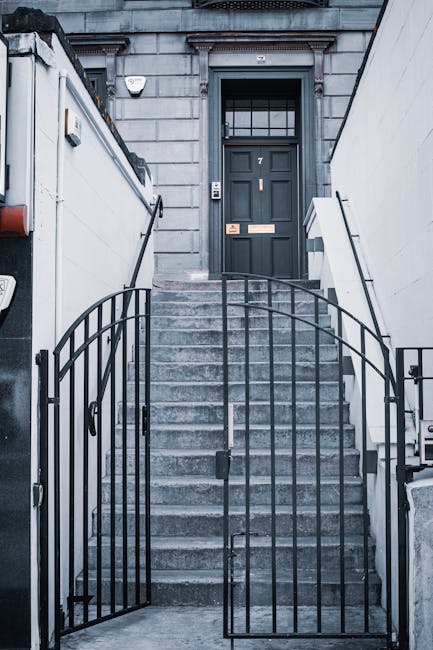 The image shows a narrow staircase inside a residential building, viewed from a doorway with the door open outward. The staircase consists of dark wooden steps leading upward, with a handrail on the l